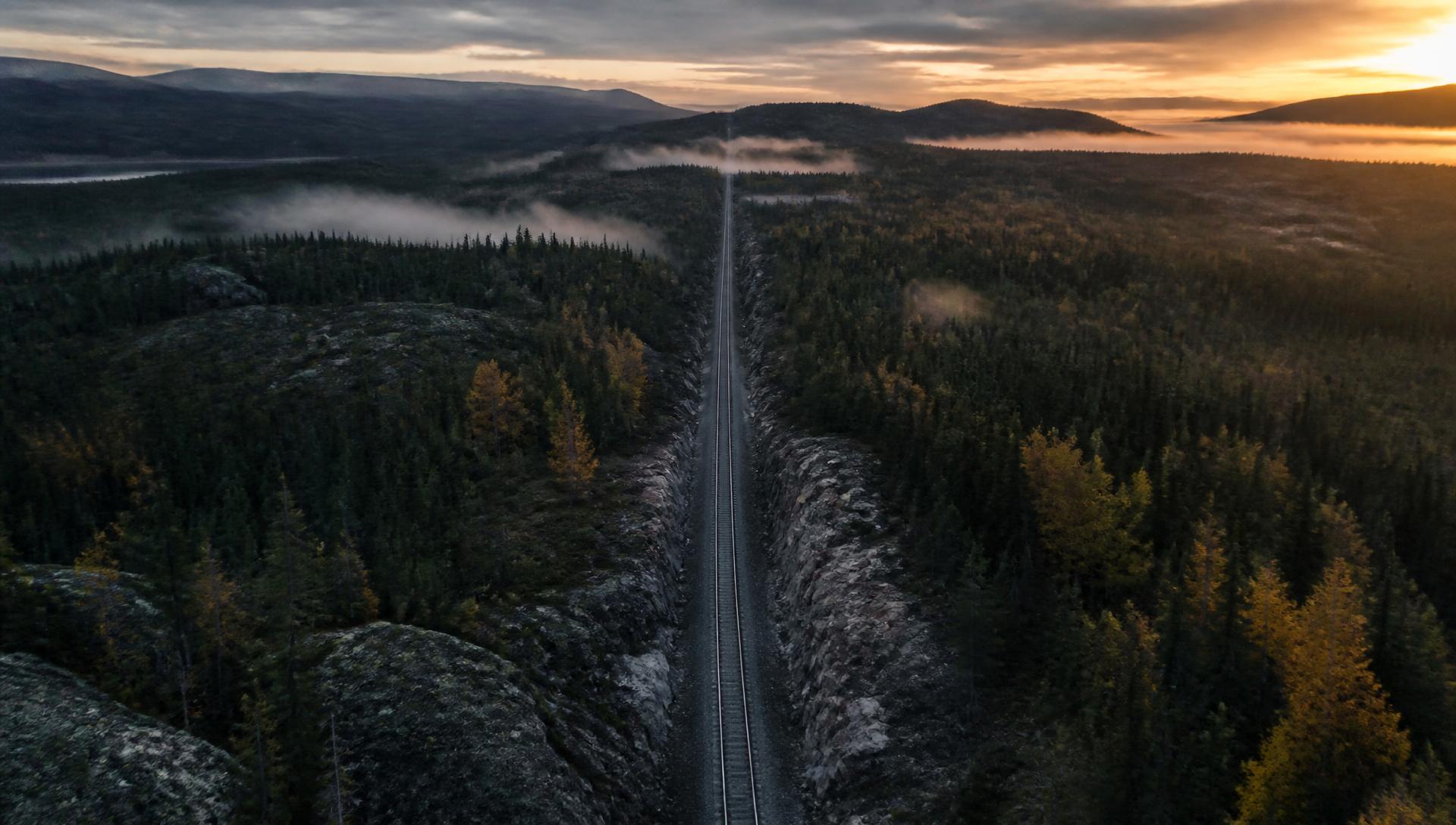 Remote rail corridor cut through boreal forest and rock at dusk